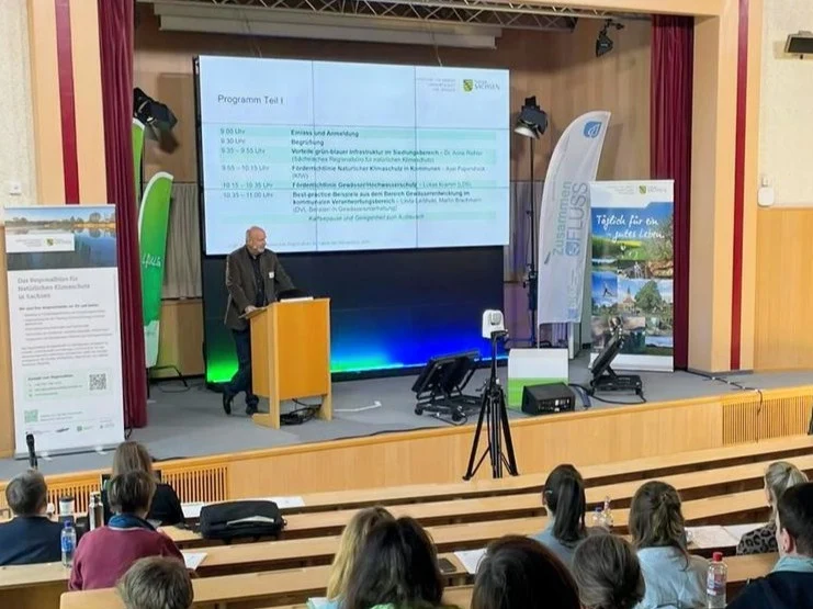Vortrag während der Fachveranstaltung „Natürlicher Klimaschutz und Klimaanpassung im Siedlungsbereich“ in der Aula der Fachschulen für Agrartechnik und Gartenbau in Dresden-Pillnitz. Die Teilnehmenden verfolgen die Präsentation im Hörsaal.